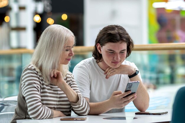 A woman and a young man look into a smartphone while sitting at a table in a cafe discussing something