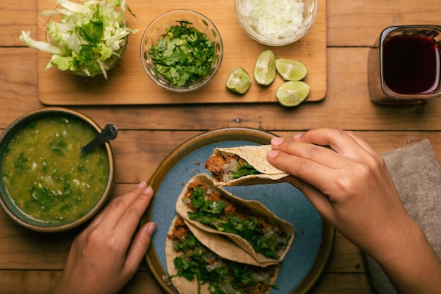 Woman39s hand holding a taco of marinated meat Plate with tacos sauce and vegetables on wooden table Top view