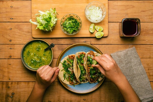 Woman39s hand holding a taco of marinated meat Plate with tacos sauce and vegetables on wooden table