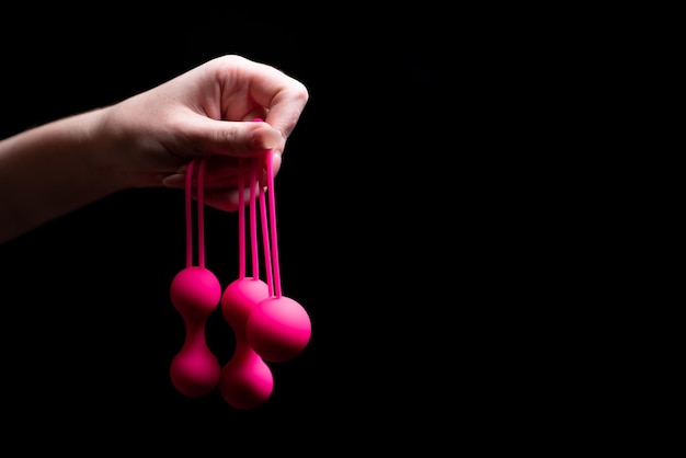 Woman39s hand holds pink Kegel balls Ben Wa balls on a black isolated background Vaginal balls in a female hand Sex toys Geisha balls Place for text Sex shop concept