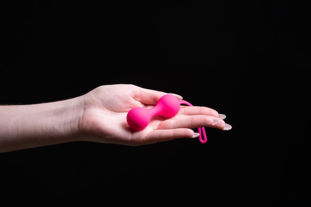 Woman39s hand holds pink kegel balls ben wa balls on a black\
isolated background vaginal balls in a female hand sex toys geisha\
balls place for text sex shop concept