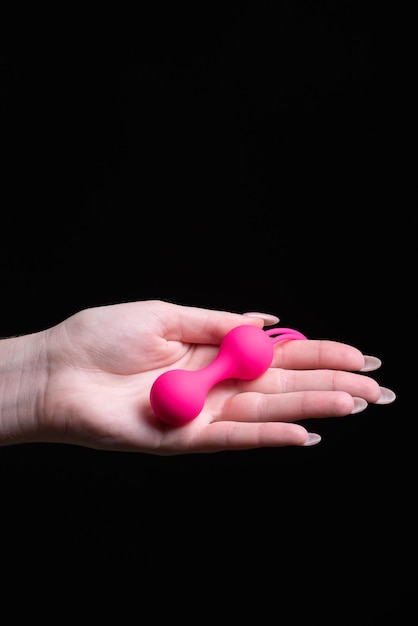 Woman39s hand holds pink kegel balls ben wa balls on a black\
isolated background vaginal balls in a female hand sex toys geisha\
balls place for text sex shop concept