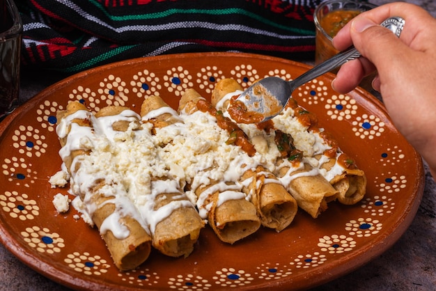 Woman39s hand spooning salsa on a plate of golden potato tacos Mexican food