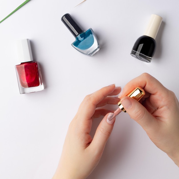 Woman39s hands brushing fingernail with colorful liquid nail polish different colors nail polish on the background