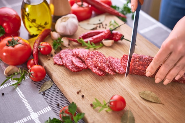 Woman39s hands cutting a salami sausage on wooden cutting board at domestic kitchen