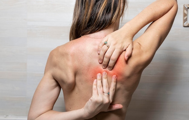 女性 39 の手が彼女の背中を赤いまたは赤い痛みのある領域に感じている、トレーニング中の肩甲骨の痛み、または理学療法士が必要な姿勢の悪さ