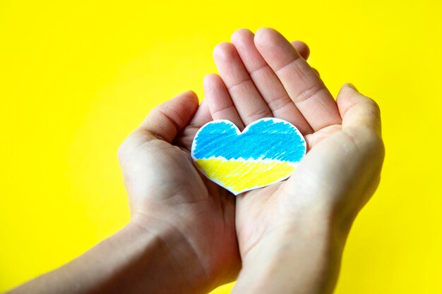 Woman39s hands holding a paper heart cut out in the colors of the Ukrainian flag on yellow background with space for copy War