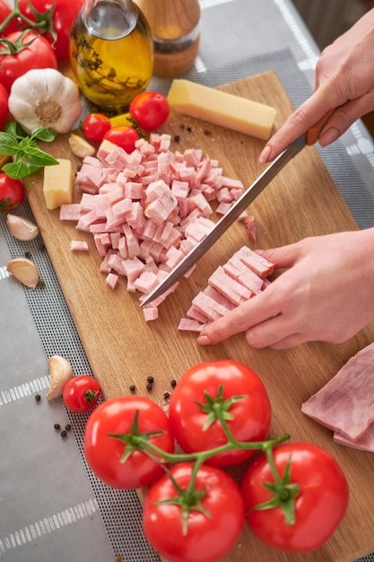 Woman39s hands slicing pancetta ham bacon on wooden cutting board at domestic kitchen