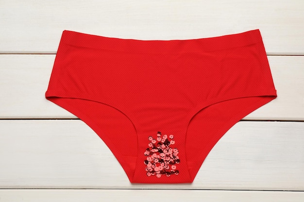 Woman39s panties with red sequins on white wooden background top view Menstrual cycle