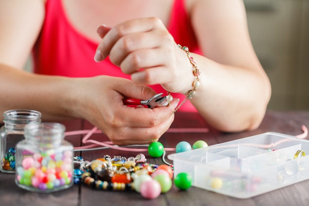 Foto le mani di una donna fanno un braccialetto con perline di plastica