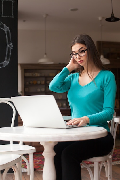 Womanfreelancer with black glasses is working with her grey laptop at the wood table