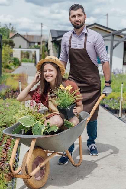 Womangardener sitting with plants in wheelbarrow with man gardener behind