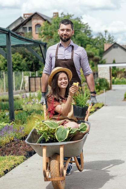 Womangardener sitting with plants in wheelbarrow with man gardener behind