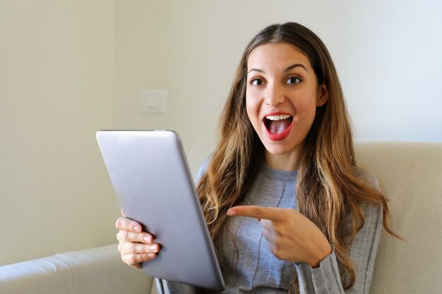 Womanpointing finger at tablet computer on sofa at home