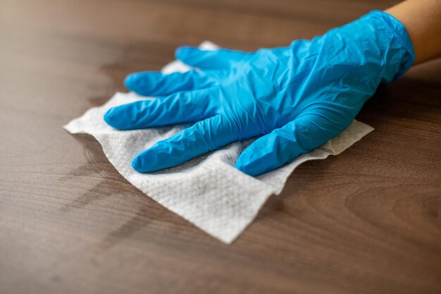 Photo womans hand in blue gloves sanitizing cleaning home office wood table surface with wet wipes