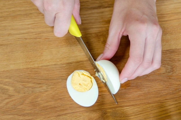 A womans hand cuts a boiled egg in half closeup a quick snack in the form of a boiled egg top view