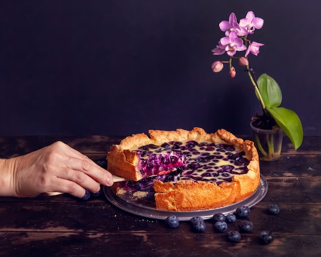 Womans hand cuts off and takes a piece of rustic shortbread pie with blueberries