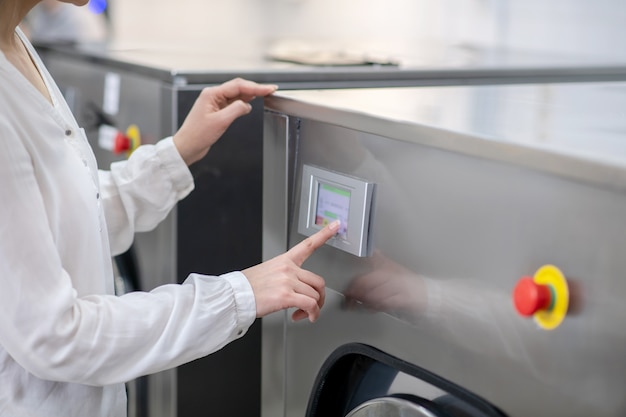 womans hand gently touching panel of washing machine, controlling her program, without face