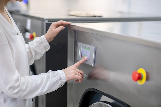 Womans hand gently touching panel of washing machine, controlling her program, without face