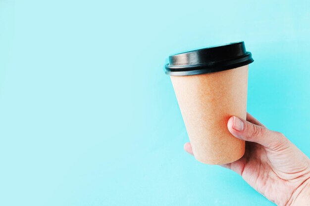 Womans hand hold takeaway coffee cup on blue background Copy space for the text Minimal concept