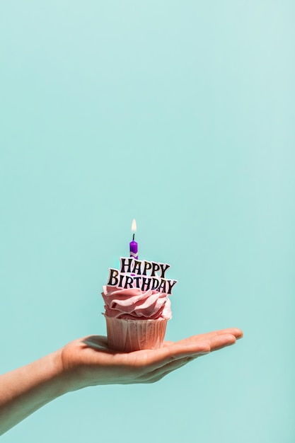 Womans hand holding birthday cupcake with candle