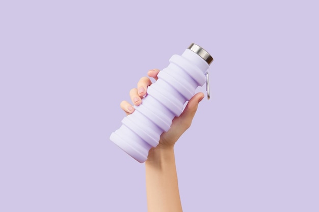 Womans hand holding collapsible reusable lilac water bottle on purple background zero waste