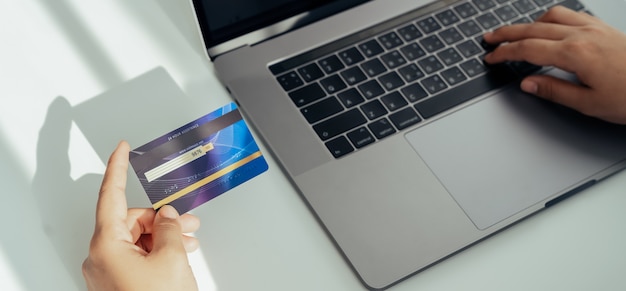 Womans hand holding a credit card and using a laptop for online shopping on a white desk