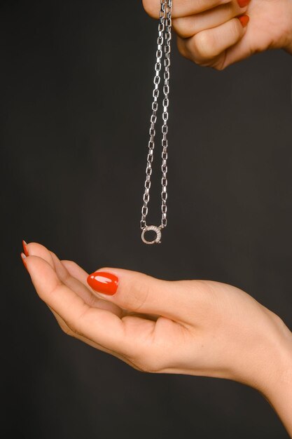 Womans hand holding a delicate silver chain necklace against a dark backdrop