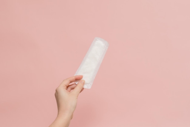 Womans hand holding sanitary pad on pink background