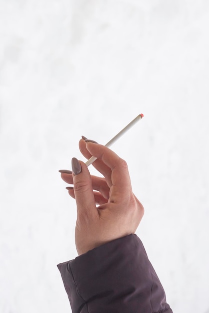 A womans hand holding a smoking cigarette against the light background of the copy space