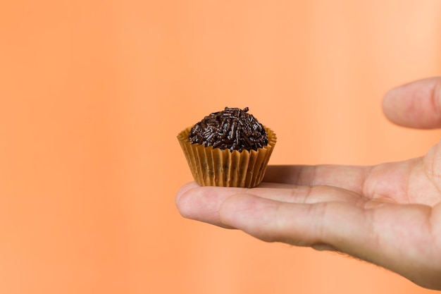 A womans hand holding a vegan brigadeiro Typical Brazilian sweet Orange background