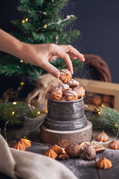 Женская рука держит печенье Picci - рождественское песочное печенье в винтажной банке на фоне еловых веток.
