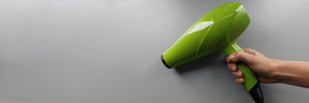 A womans hand holds a green hair dryer closeup