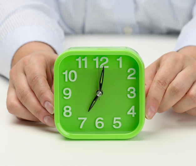 womans hand holds a green square alarm clock the clock shows seven in the morning Wake up early start the day