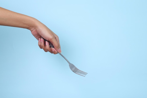 Womans hand holds a metal fork on a blue background