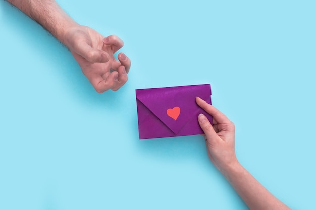 A womans hand holds purple envelope for Valentines Day and give it to man hand that expressing