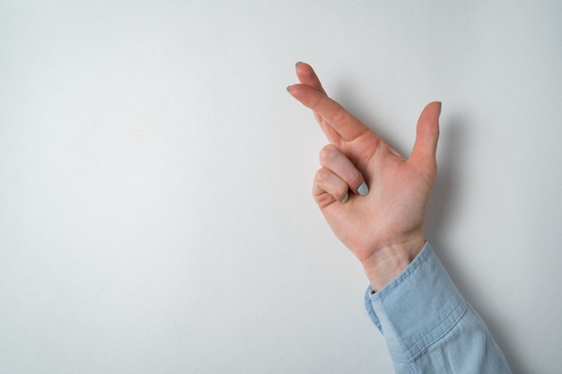 Womans hand making fingers crossed on white wall. Gesture for luck.