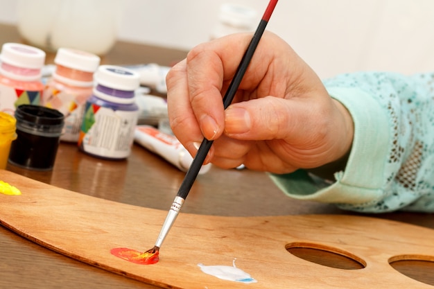 A womans hand mixing red and yellow paints on the palette