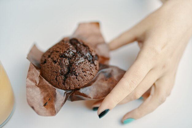 Womans hand picks up chocolate cupcake from table sweet muffin on white background dark chocolate de...