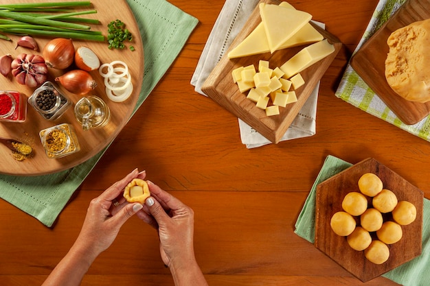木製のテーブルの上にブラジルのチーズ詰めコロッケbolinhadequeijoを準備する女性の手上面図