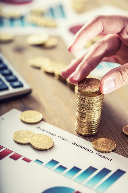 Womans hand put euro coins with a growth effect. Still life with business plan cackulator and euro currency.