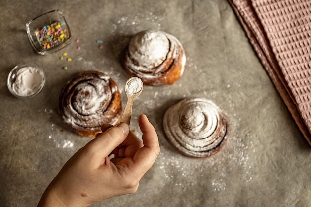 Womans hand sprinkles icing sugar on fresh baked cinnamon buns