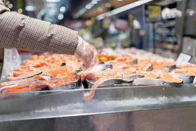 Womans hand in the supermarket with a plastic glove taking\
slices of cut salmon