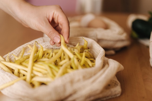 Womans hand take a green beans from reusable grocery bag with vegetables on a table at home mesh