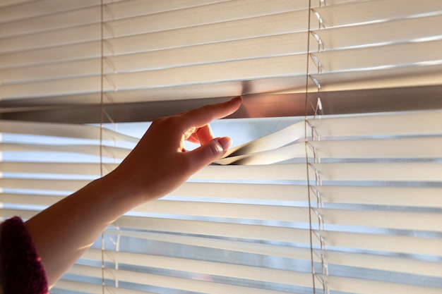 Womans hand taking a peak through the window blinds