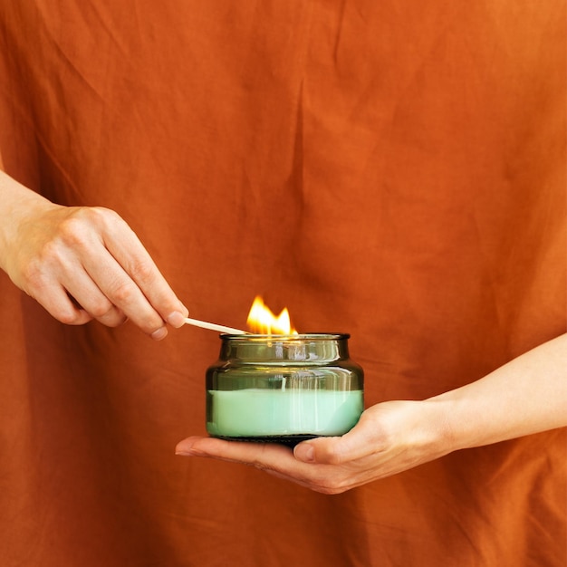 Womans hand uses match to light aromatic candle in glass jar Wellness and physical emotional health