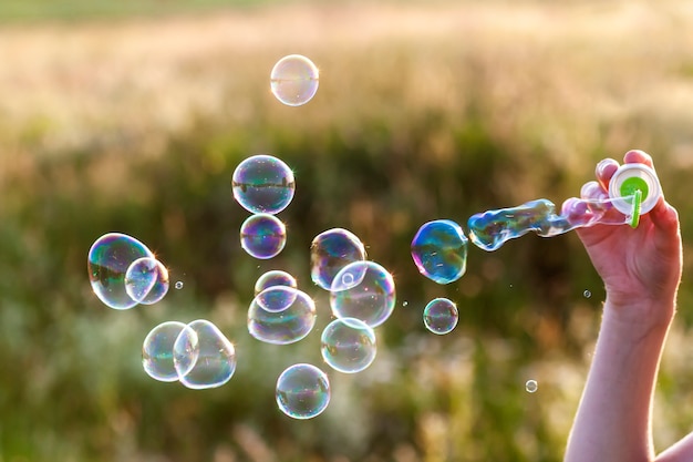 Womans hand with blowing colorful soap bubbles at sunset.