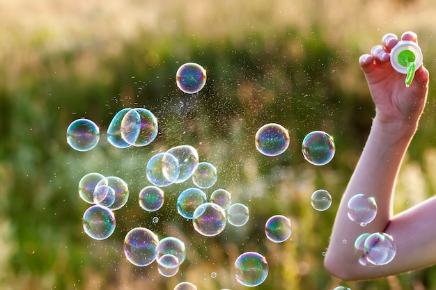 Photo womans hand with blowing colorful soap bubbles at sunset.