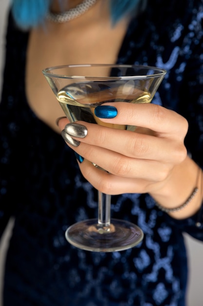 Mano della donna con il manicure che tiene il bicchiere di sfondo di vermouth. design per unghie argento notte oscura festa.