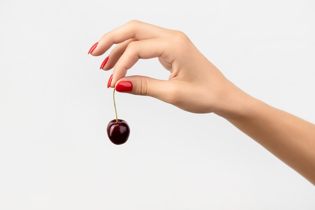 Womans hand with red manicure holding cherry